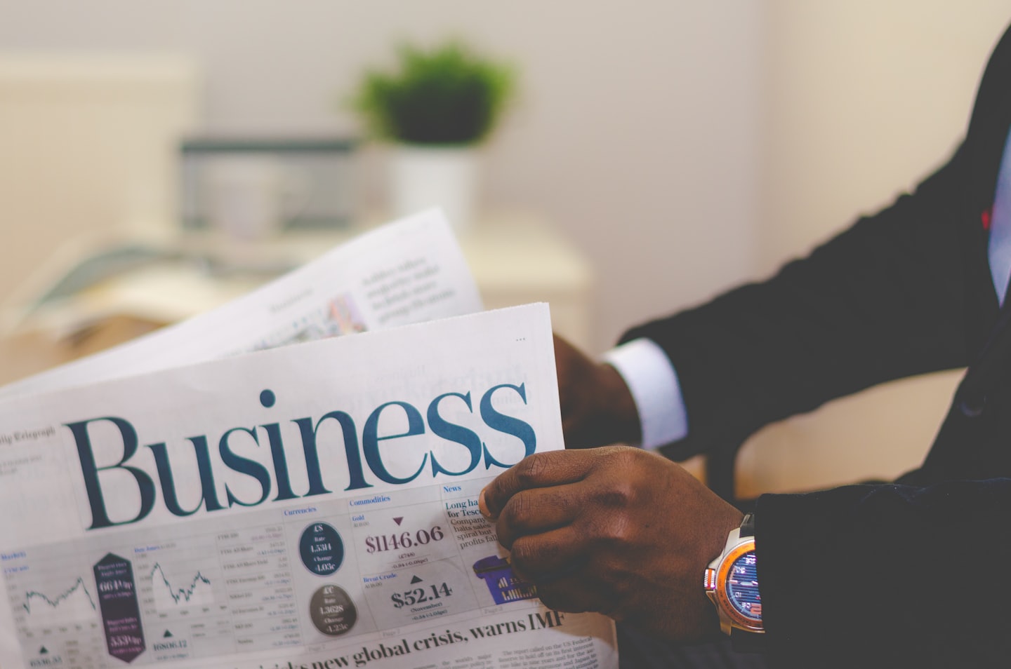 Mãos de um homem de terno segurando um jornal com título grande dizendo "Business".